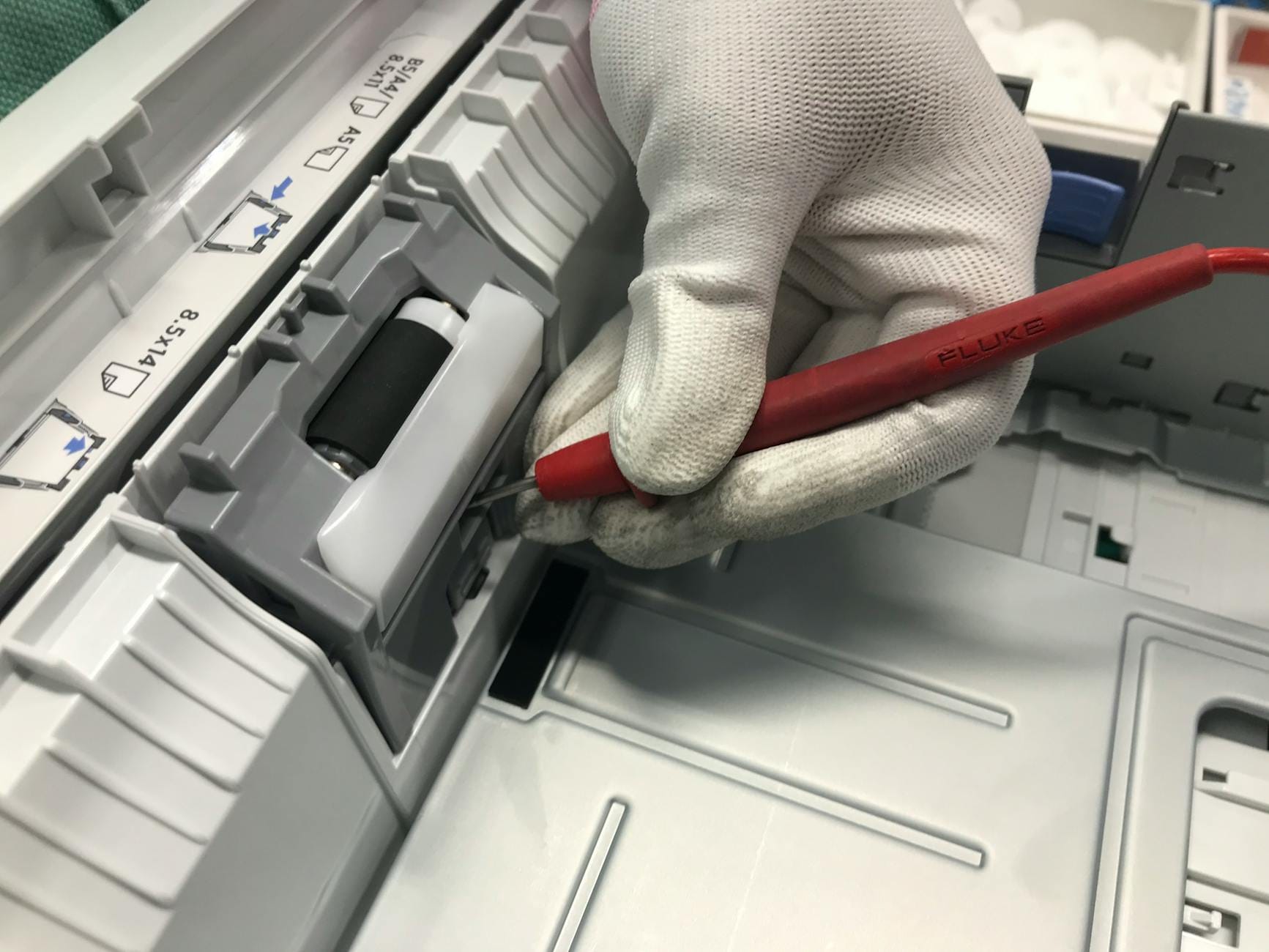 Ręka w rękawiczce czyści wnętrze drukarki laserowej czerwonym narzędziem