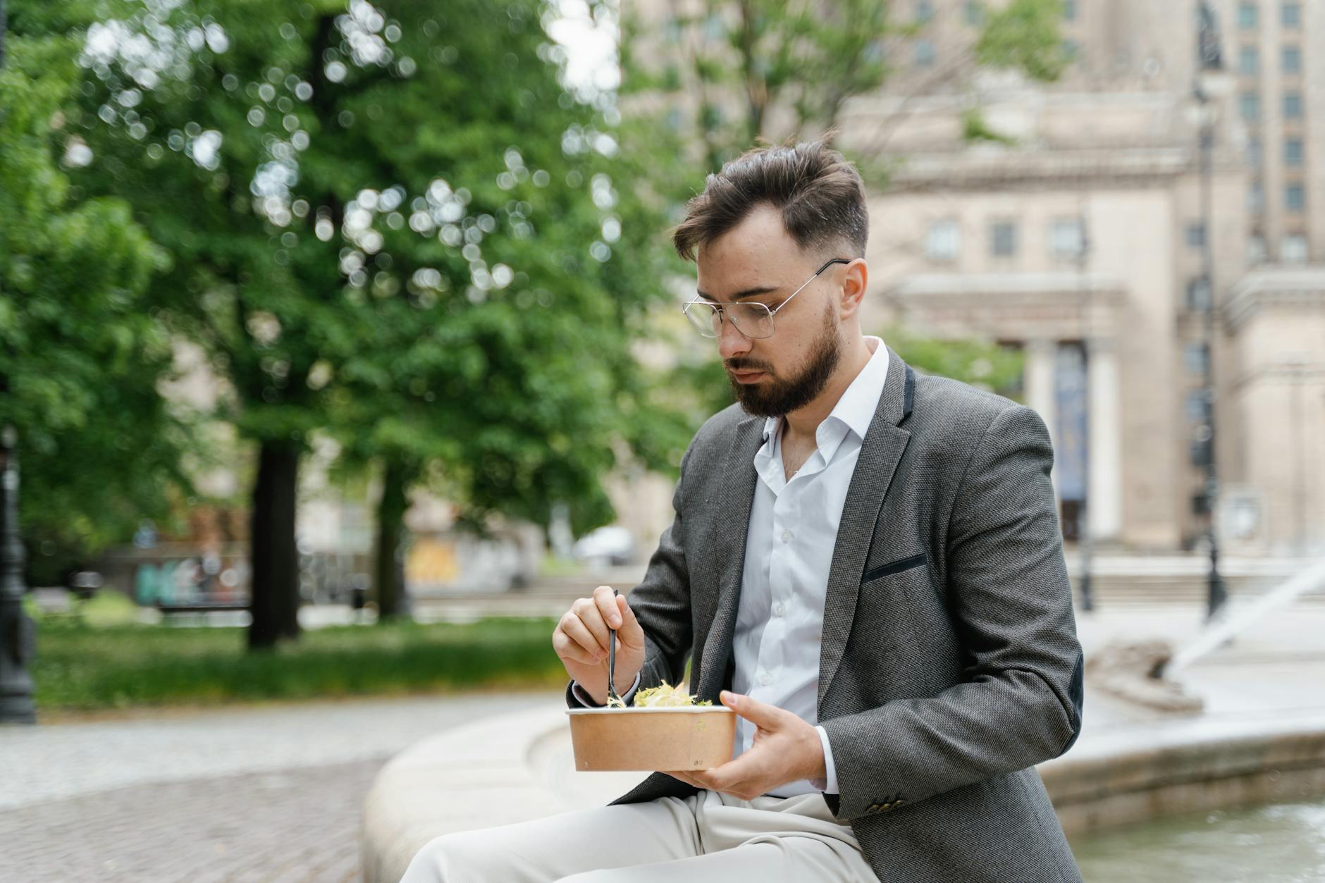 Mężczyzna w garniturze je lunch na ławce w miejskim parku