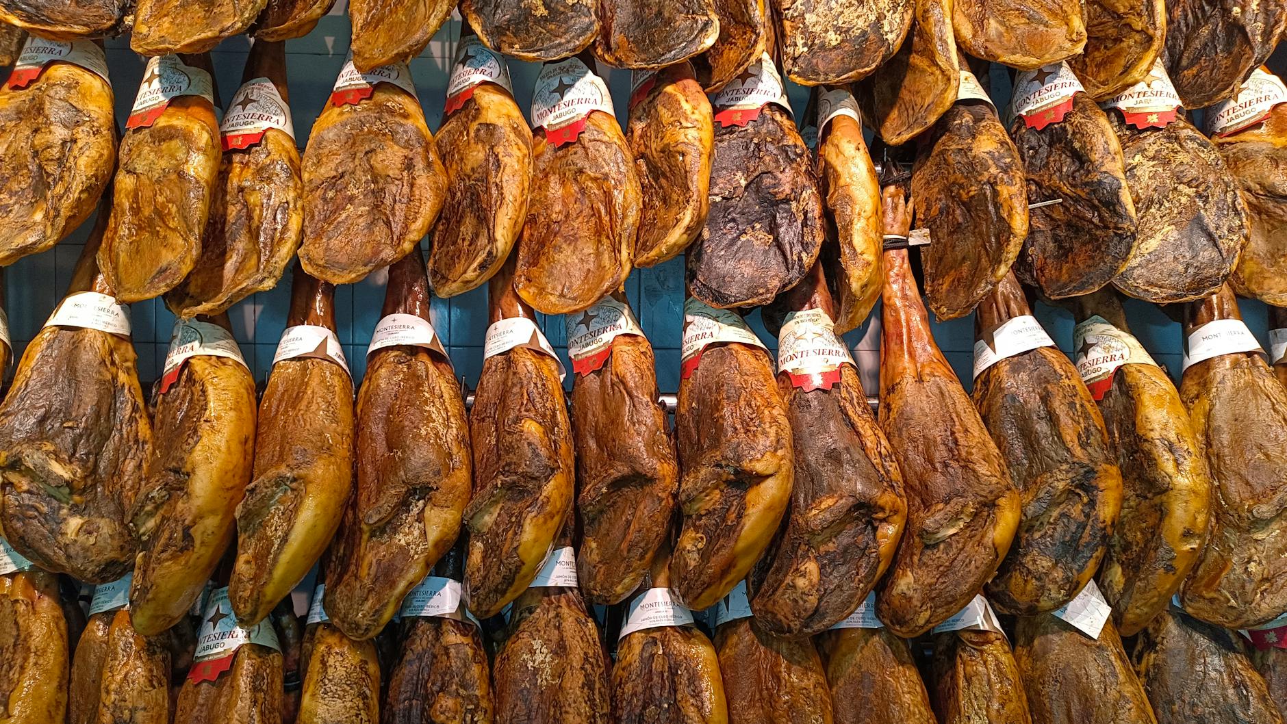 Jak wybrać hiszpańską szynkę premium: przewodnik po jamón serrano i jamón ibérico dla początkujących Wiszące w markecie kawały jamón ibérico na stoisku w Hiszpanii