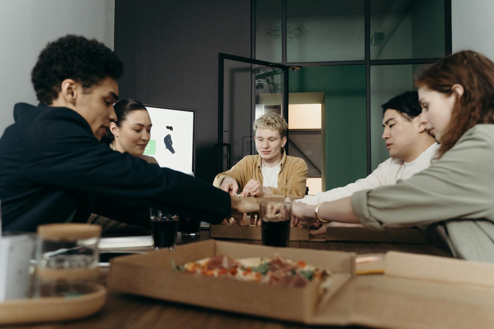 Zespół współpracowników je pizzę podczas przerwy w nowoczesnym biurze