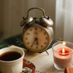 Kofeina a jakość fazy deep sleep: o której godzinie wypić ostatnią filiżankę, by nie psuć snu? Zegar vintage, filiżanka kawy i świeca na stole